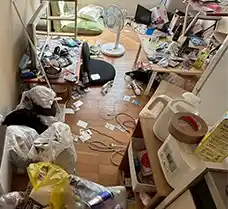 札幌市東区のロフト付き1DKアパートにて、退去前に残された家財道具や生活ゴミが床一面に散乱している状態。ロフトへ続くハシゴの周辺にも荷物が積み重なり、自力での片付けが困難な作業前の様子。